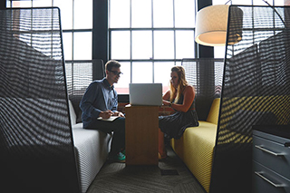 Man and woman sharing a booth and working on a laptop together