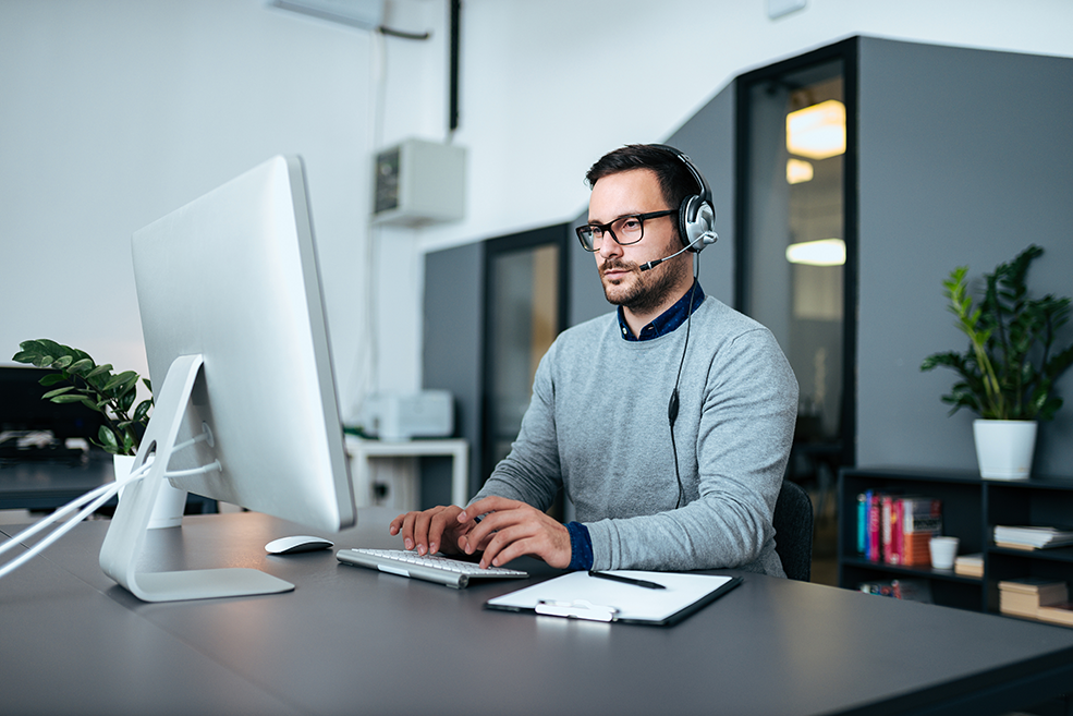Jeune homme spécialiste informatique portant un casque et travaillant sur des analyses d’infrastructure sur un ordinateur.